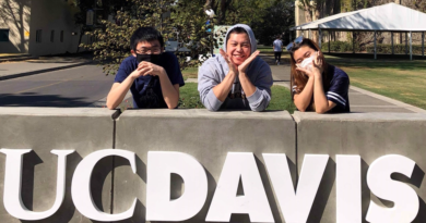 Three UC Davis students lean on a UCD sign